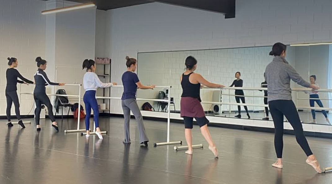 Photo of dancers at a ballet barre with their leg out in a tendu. 